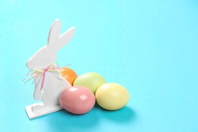 Photo of Cute wooden Easter bunny and dyed eggs on color background, space for text