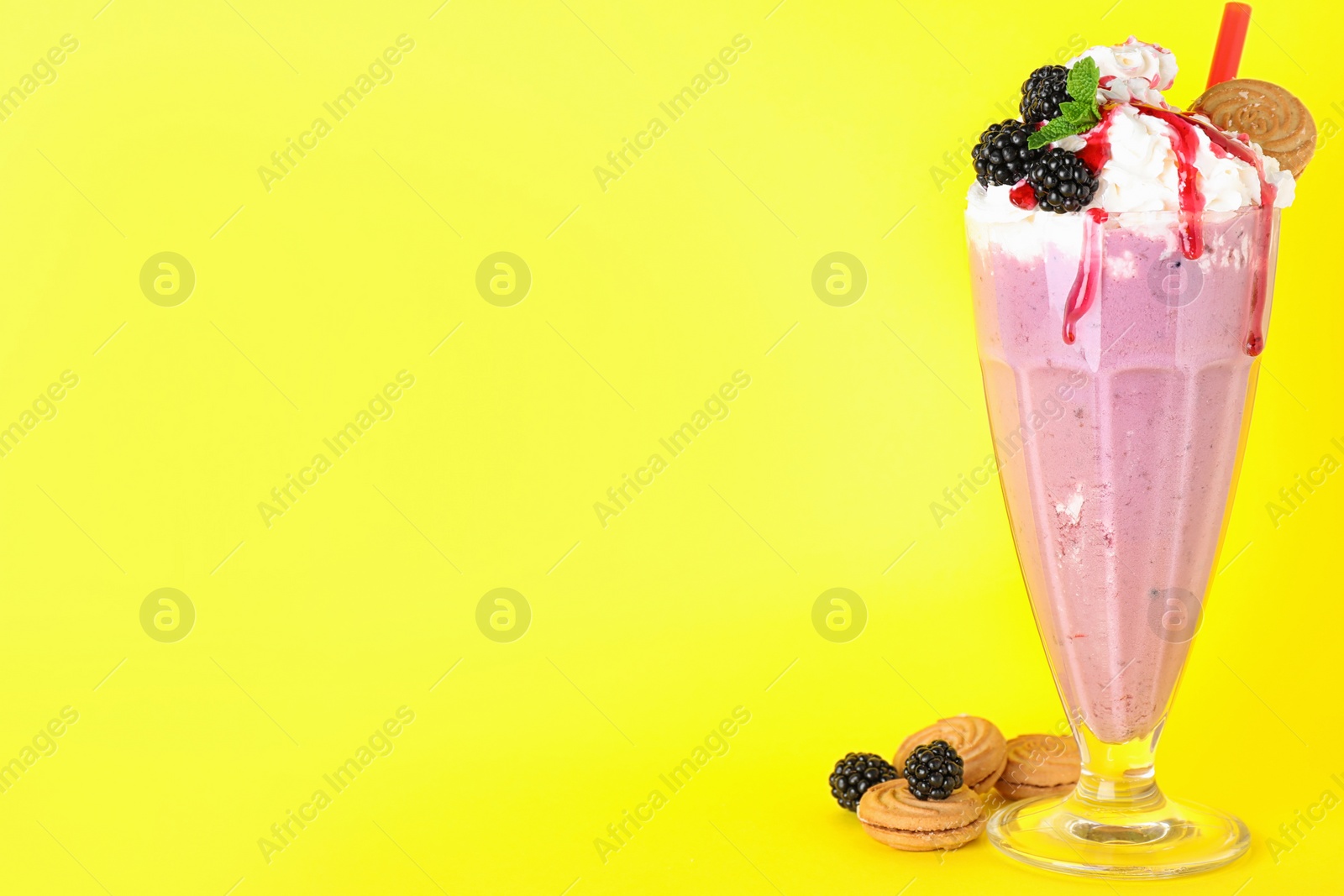 Photo of Tasty milk shake in glass, blackberries and cookies on yellow background. Space for text