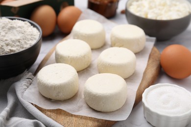 Photo of Uncooked cottage cheese pancakes and different ingredients on white table, closeup