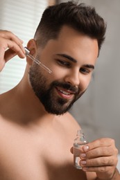 Handsome man applying cosmetic serum onto his face in bathroom
