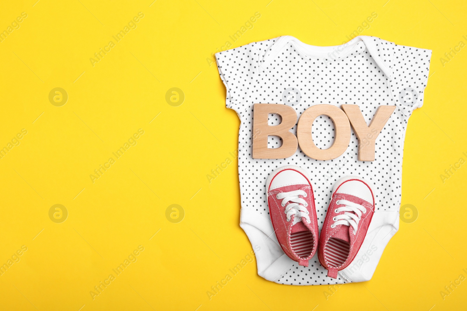 Photo of Child's bodysuit, word Boy made with wooden letters and booties on yellow background, top view. Space for text