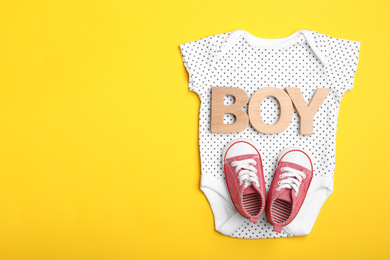 Photo of Child's bodysuit, word Boy made with wooden letters and booties on yellow background, top view. Space for text