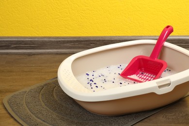 Photo of Cat tray with crystal litter and scoop on floor near yellow wall