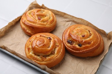 Delicious rolls with raisins on white tiled table, closeup. Sweet buns