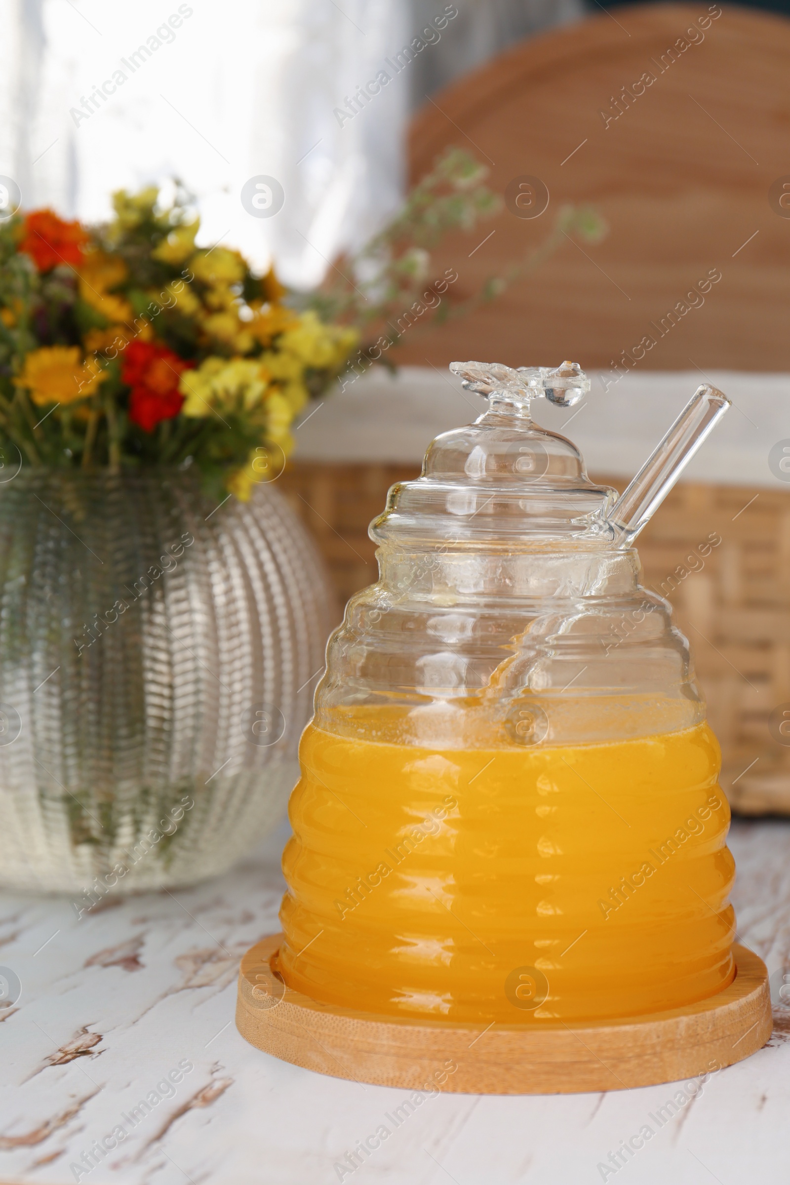 Photo of Delicious fresh honey and beautiful flowers on white wooden table indoors