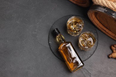 Whiskey with ice cubes in glasses, bottle and wooden barrel on black table, top view. Space for text