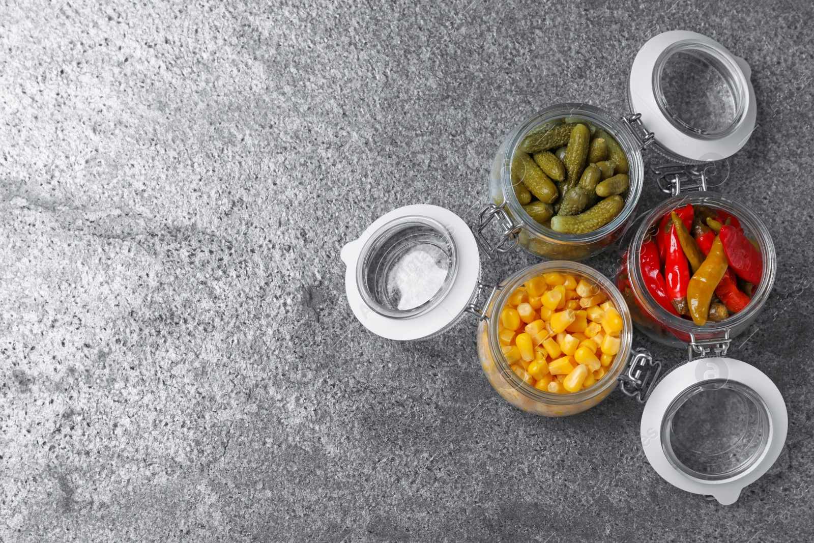 Photo of Flat lay composition with jars of pickled vegetables on grey table. Space for text