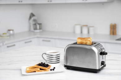 Modern toaster and tasty breakfast on white marble table in kitchen