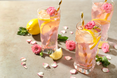 Delicious refreshing drink with rose flowers and lemon slices on light grey table