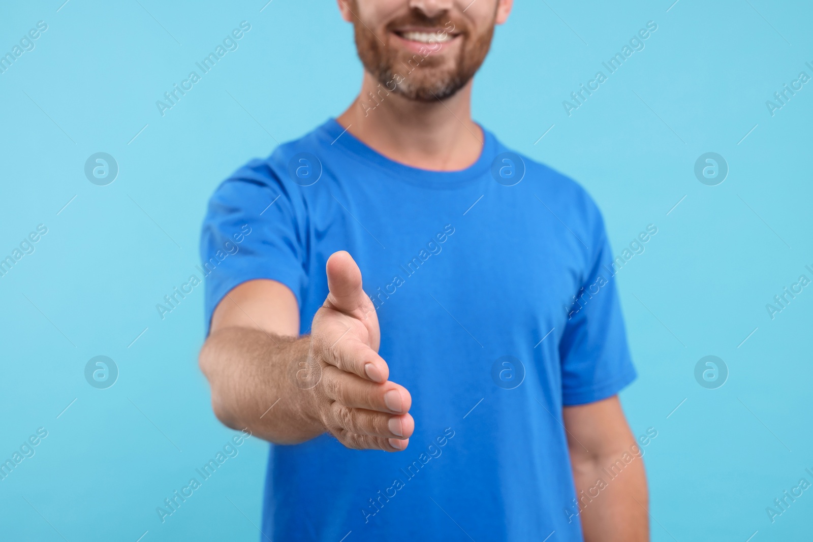 Photo of Man welcoming and offering handshake on light blue background, closeup