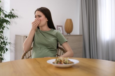 Photo of Young woman feeling nausea while seeing food at wooden table indoors. Toxicosis during pregnancy