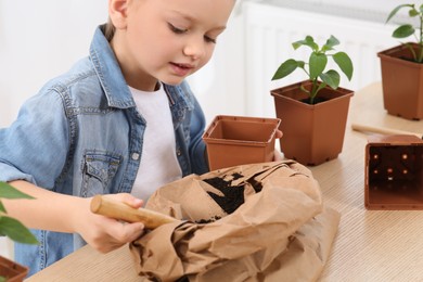 Cute little girl planting seedling into pot at wooden table indoors