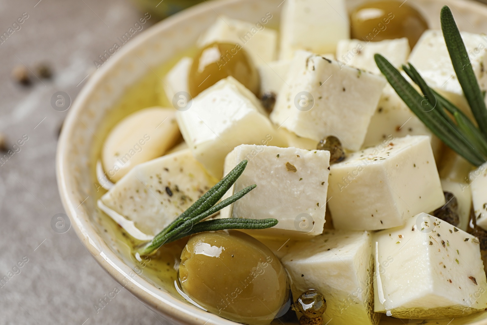 Photo of Pickled feta cheese in bowl on light brown table, closeup