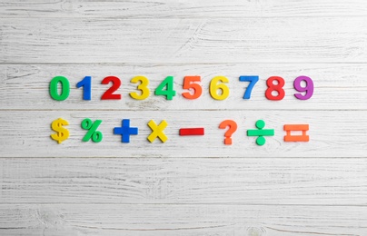 Colorful magnetic numbers and math symbols on white wooden background, flat lay