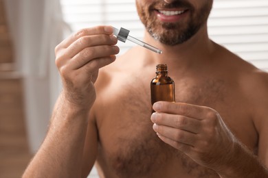 Smiling man with cosmetic serum indoors, selective focus