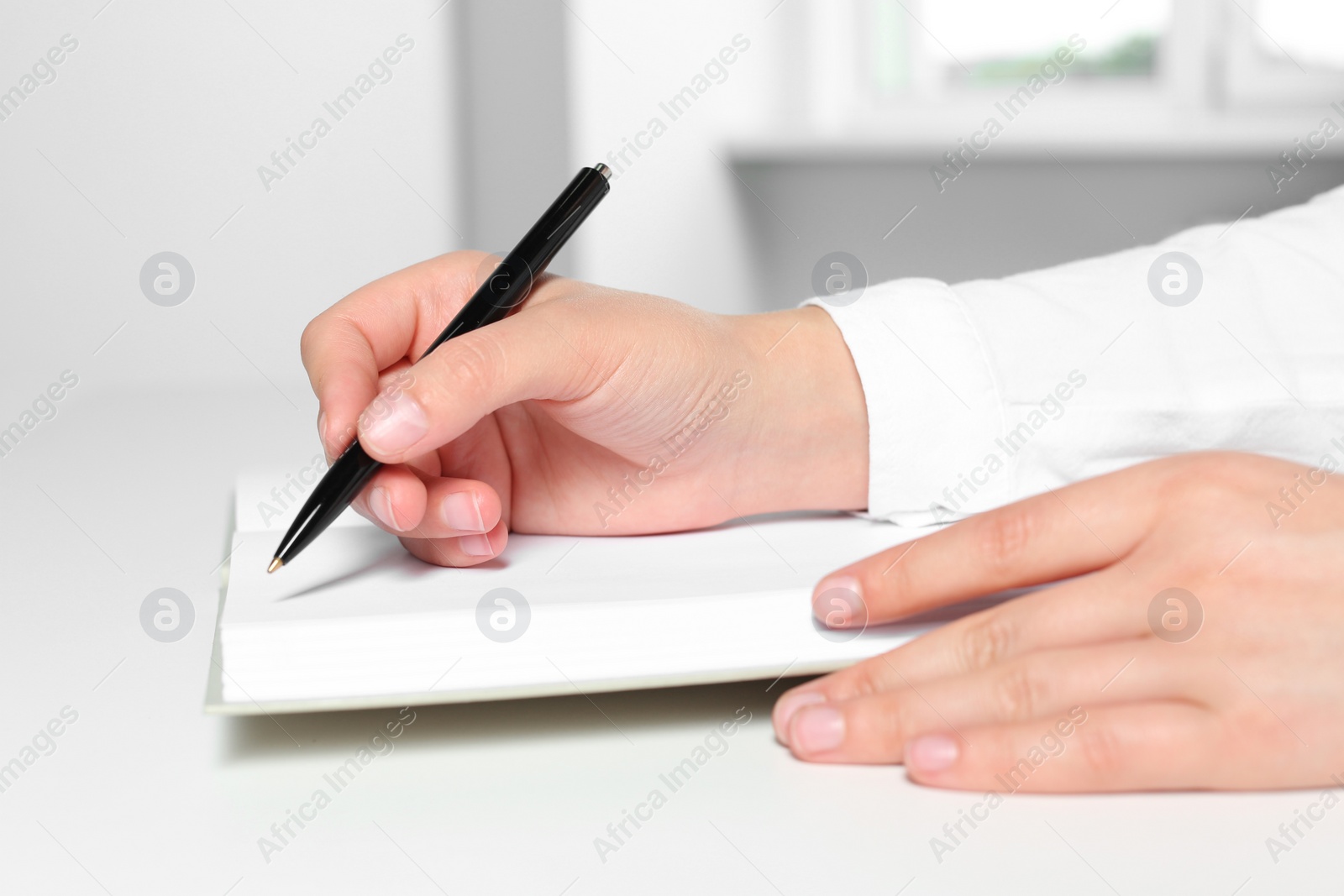 Photo of Woman writing in notebook at white table in office, closeup