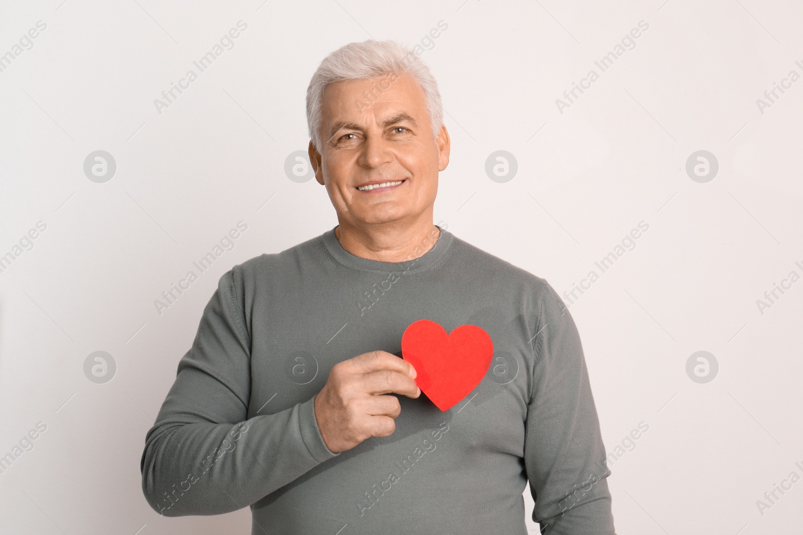 Photo of Happy mature man holding red paper heart on white background