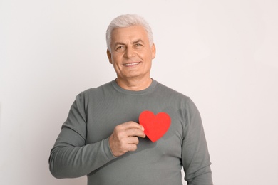 Photo of Happy mature man holding red paper heart on white background