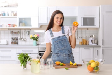 Photo of Young woman preparing lemonade on table in kitchen. Natural detox drink