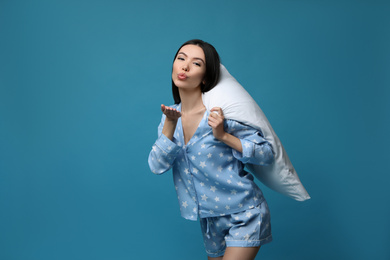 Photo of Beautiful Asian woman with pillow blowing kiss on blue background. Bedtime