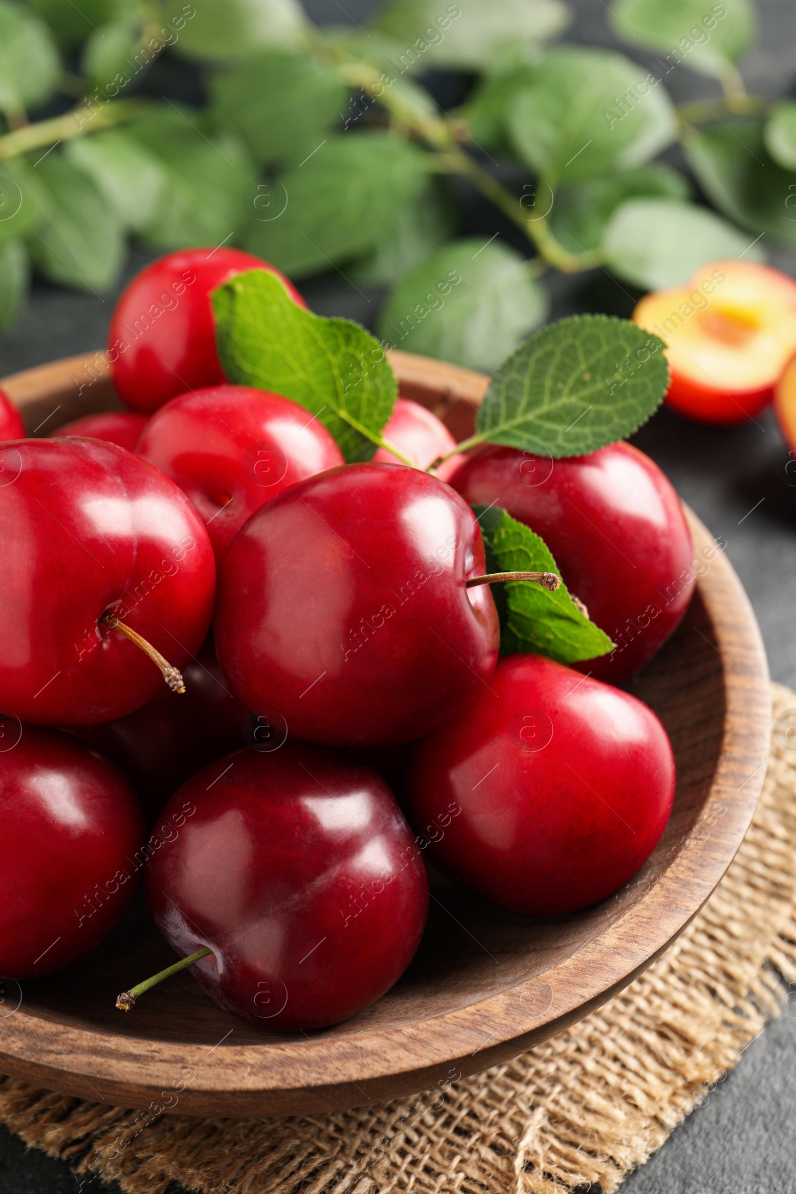 Photo of Delicious ripe cherry plums with leaves on black table, closeup