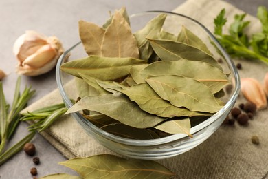 Photo of Aromatic bay leaves in glass bowl, different herbs and spices on table, closeup