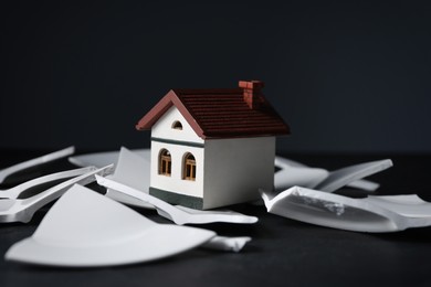Photo of House model and broken dishes on black table depicting destruction after earthquake