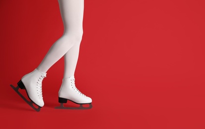 Woman in elegant white ice skates on red background, closeup of legs. Space for text