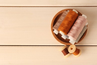 Photo of Bowl with color sewing threads on wooden table, flat lay. Space for text