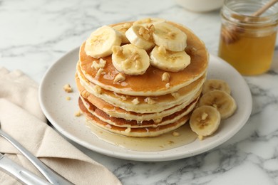 Photo of Delicious pancakes with bananas, walnuts and honey on white marble table, closeup