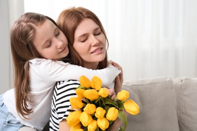 Photo of Mother and her cute daughter with bouquet of yellow tulips at home. Space for text