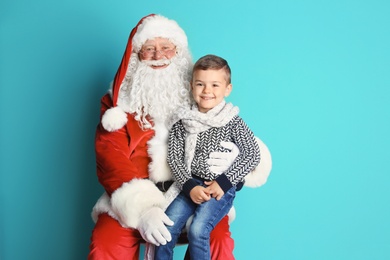 Photo of Little boy sitting on authentic Santa Claus' lap against color background