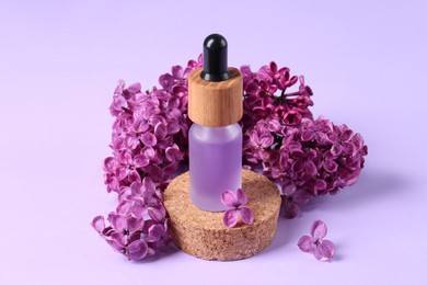 Photo of Bottle with essential oil and lilac flowers on violet background