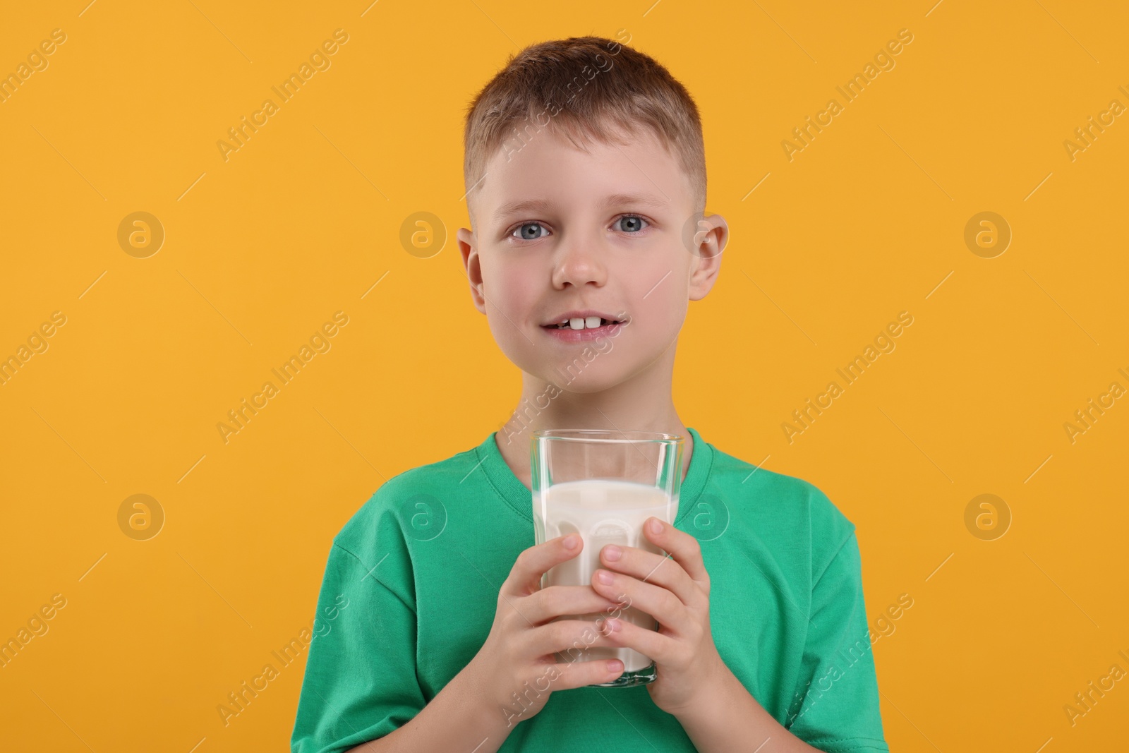 Photo of Cute boy with glass of fresh milk on orange background