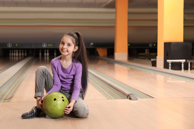 Photo of Little girl with ball in bowling club. Space for text