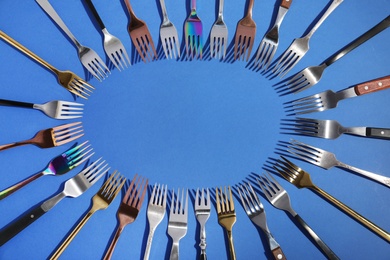 Photo of Frame made of different forks on blue background, top view. Space for text