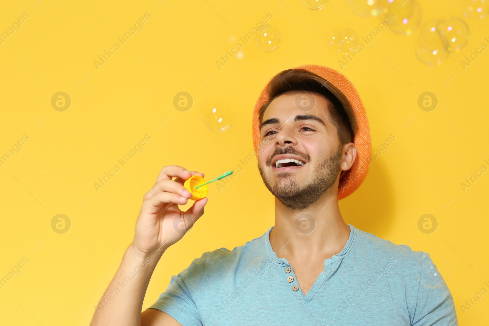 Photo of Young man blowing soap bubbles on color background. Space for text