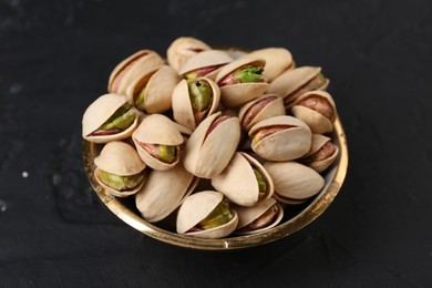 Photo of Tasty pistachios in bowl on black table, closeup