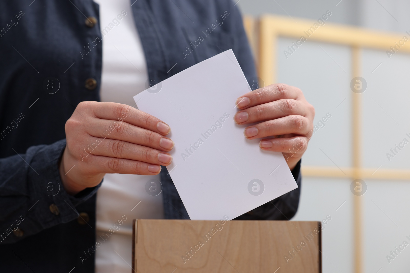 Photo of Woman putting her vote into ballot box on blurred background, closeup