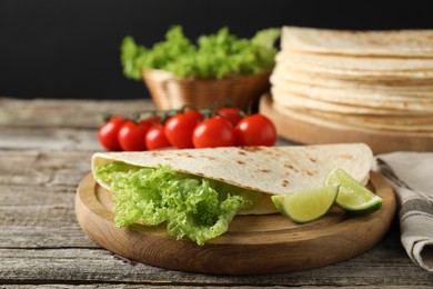 Photo of Tasty homemade tortillas, lettuce, lime and tomatoes on wooden table