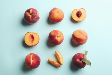 Fresh ripe peaches and green leaves on light blue background, flat lay