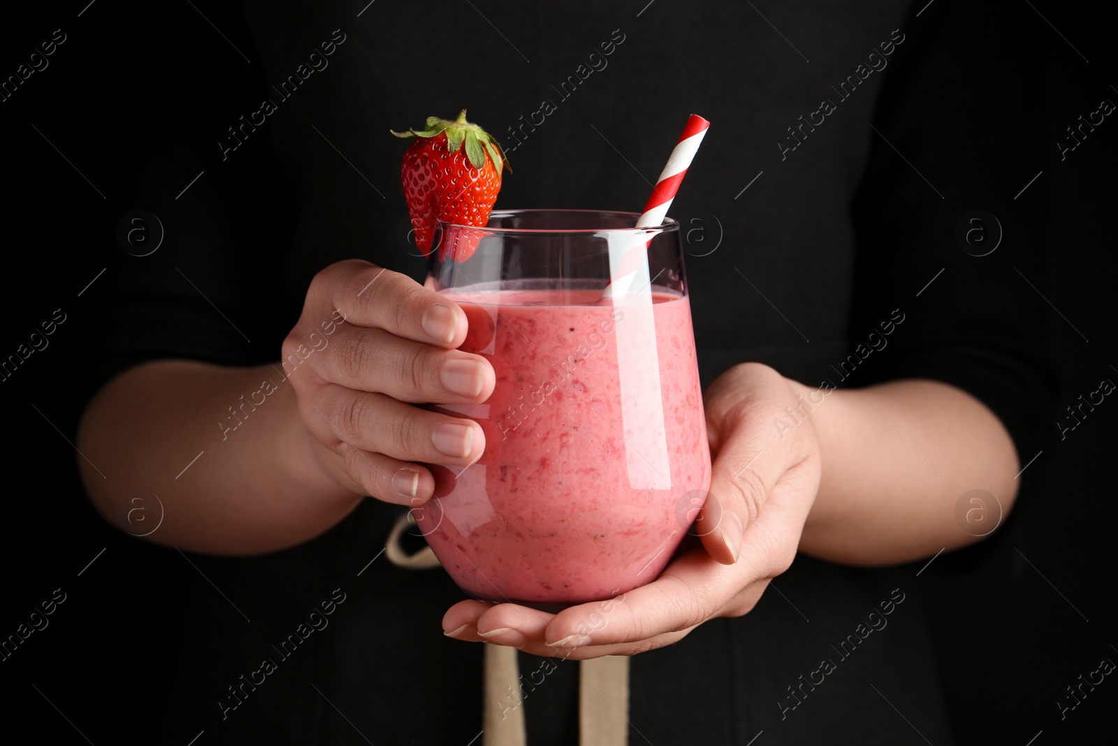 Photo of Woman holding tasty strawberry smoothie on black background, closeup