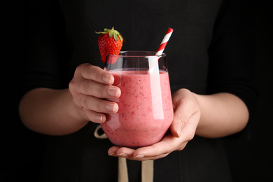 Photo of Woman holding tasty strawberry smoothie on black background, closeup