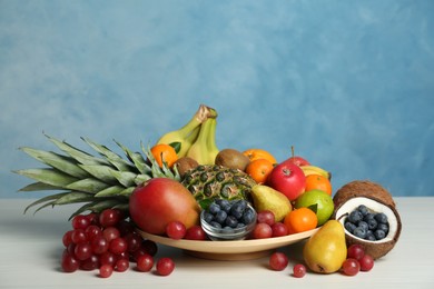 Photo of Assortment of fresh exotic fruits on white wooden table against light blue background