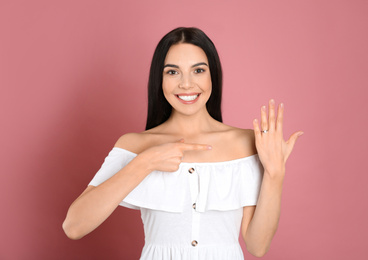 Photo of Happy young woman wearing beautiful engagement ring on pink background