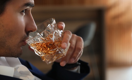 Young man with glass of whiskey indoors, closeup