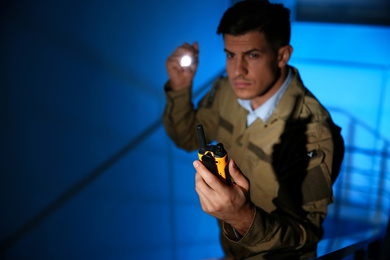 Photo of Professional security guard with portable radio set in dark room, focus on hand