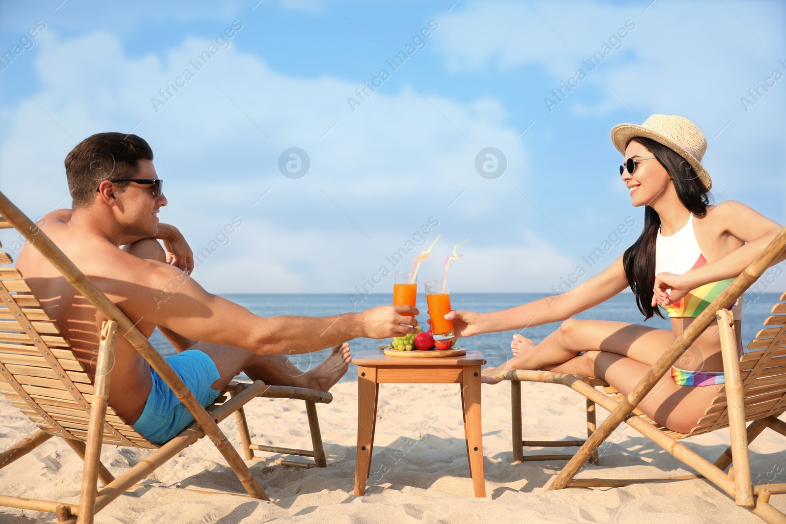 Photo of Couple with drinks resting on sunny beach at resort