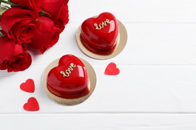 Photo of St. Valentine's Day. Delicious heart shaped cakes and beautiful roses on white wooden table, above view. Space for text