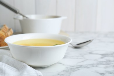Photo of Delicious bouillon in bowl on white marble table, closeup